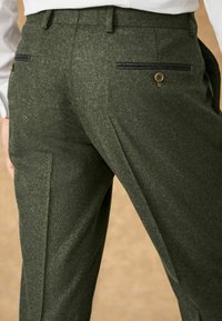 Pantalons en mélange de laine verte avec une finition texturée, dotés de deux poches arrière avec des accents noirs et un détail de bouton.