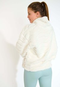 Maglione bianco, in peluche, di grandi dimensioni con colletto alto e motivo di texture ondulata. Abbinate a leggings blu chiaro.