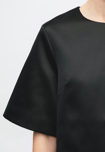 Sort satinbluse med rund halsudskæring og korte ærmer. Stoffet har en glat tekstur, der subtilt reflekterer lys uden mønstre.