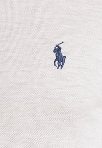 Ljusgrå bomullspolo med en texturerad stickning; har en liten marinblå broderad polo-logotyp på vänster bröst.