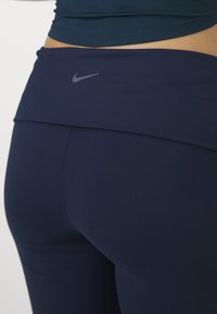Tamno plave tajice visokog struka za sport, glatke teksture s diskretnim Nike logom na pojasu. Prikaz izbliza stražnje strane.