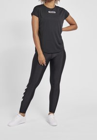 Black athletic top with a logo, paired with black leggings featuring a white zigzag pattern on the side. Completed with white sneakers.