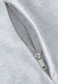 Gray fabric with a textured weave features a silver zipper, partially open, showcasing metallic teeth and a flat pull tab.