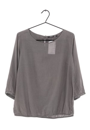 Szara luźna bluzka z rękawami do połowy łokcia, okrągłym dekoltem i marszczonym dołem, zawieszona na czarnym metalowym wieszaku na białym tle.