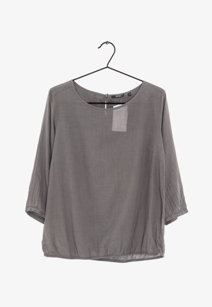 Szara luźna bluzka z rękawami do połowy łokcia, okrągłym dekoltem i marszczonym dołem, zawieszona na czarnym metalowym wieszaku na białym tle.