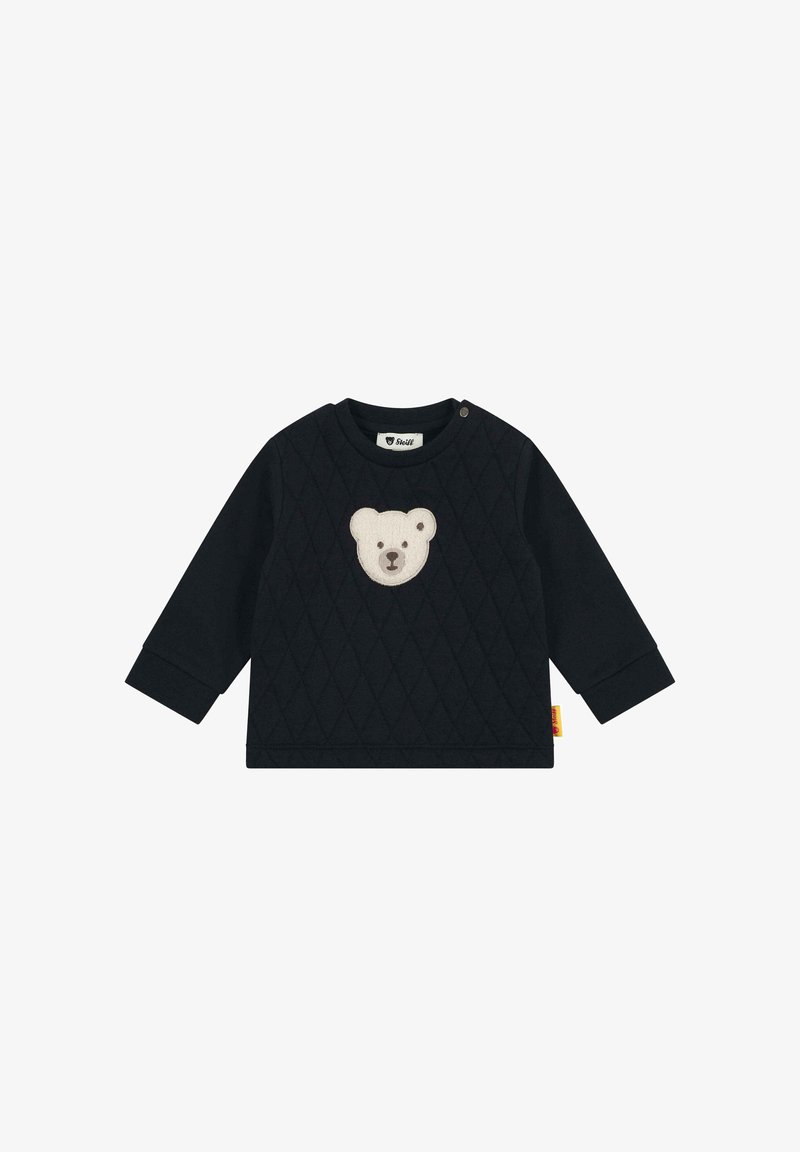 Camiseta negra acolchada de manga larga para bebé con un parche de la cara de un oso de peluche beige en el pecho y un botón de presión en el hombro.