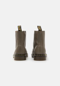 Botas de tobillo de cuero gris con punta redonda, costuras amarillas y tiradores distintivos en la parte posterior, que cuentan con una suela de goma gruesa.