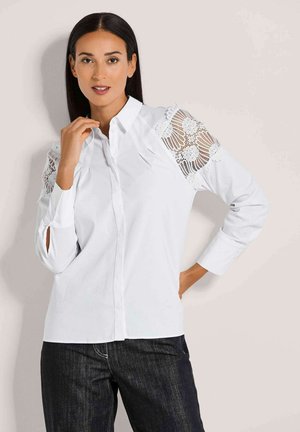 Witte blouse met kantaccenten op de schouders, lange mouwen en een klassieke kraag. Glad textuur met een getailleerde pasvorm.