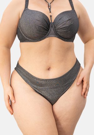 Woman wearing a dark gray metallic bikini, standing with hands relaxed at sides against a plain light background.