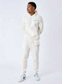Conjunto de sudadera y pantalones de chándal blancos con el logo "PROJECT X PARIS". Tejido suave, puños acanalados y un bolsillo frontal. Llevado con zapatillas blancas.