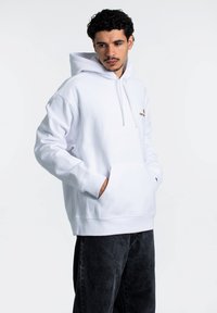Sudadera blanca de algodón, con un bolsillo tipo canguro, capucha con cordón y pequeño logo bordado en naranja en el pecho.