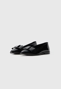 Pantofi plat din piele sintetică neagră, cu vârf ascuțit, având un accent dintr-un fundiță texturată neagră în față și un design cu toc mic.