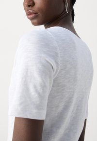 White, short-sleeve t-shirt in a lightweight, textured fabric, featuring a rounded neckline and subtle variations in weave.