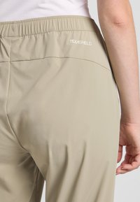 Beige lichtgewicht broeken met een elastische tailleband. Beschikt over een gladde textuur en een wit "TEXASHIELD" logo op de achterkant.