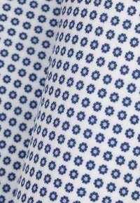 Tkanina bawełniana z powtarzającym się wzorem małych niebieskich kształtów kwiatowych na białym tle, o drobnej fakturze i gładkim wykończeniu.