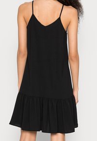 Czarna sukienka bez rękawów z dekoltem w kształcie litery V, z falbaną na dole i gładką teksturą materiału. Prosty wzór, średnia długość i minimalne detale.