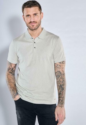 Light grey polo shirt with a subtle zigzag texture, short sleeves, three-button placket, and black buttons. Worn with dark pants.