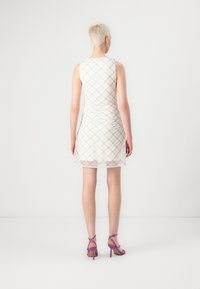Vestido blanco sin mangas con un patrón de cuadros y textura fruncida; combinado con sandalias moradas de tira. Fondo liso.