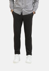 Pantalons noirs avec une coupe ajustée, ornés de manches retroussées. Associés à des baskets blanches et une chemise à carreaux noire et blanche à boutons.