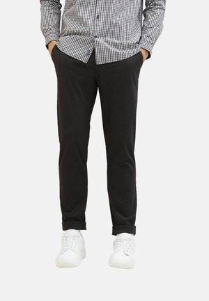 Black trousers with a slim fit, featuring rolled cuffs. Paired with white sneakers and a black and white checkered button-up shirt.