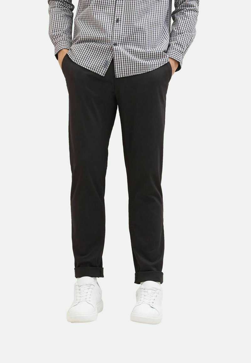 Pantalons noirs avec une coupe ajustée, ornés de manches retroussées. Associés à des baskets blanches et une chemise à carreaux noire et blanche à boutons.