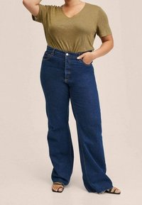 Olijfgroene V-hals T-shirt gecombineerd met hoge taille, donkerblauwe wijde jeans met voorzakken en knoopsluiting.