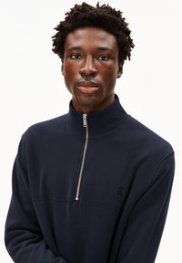 Sudadera con cremallera de color navy, fabricada con un material suave, que presenta un cuello alzado, cremallera plateada y un logo bordado en el pecho.