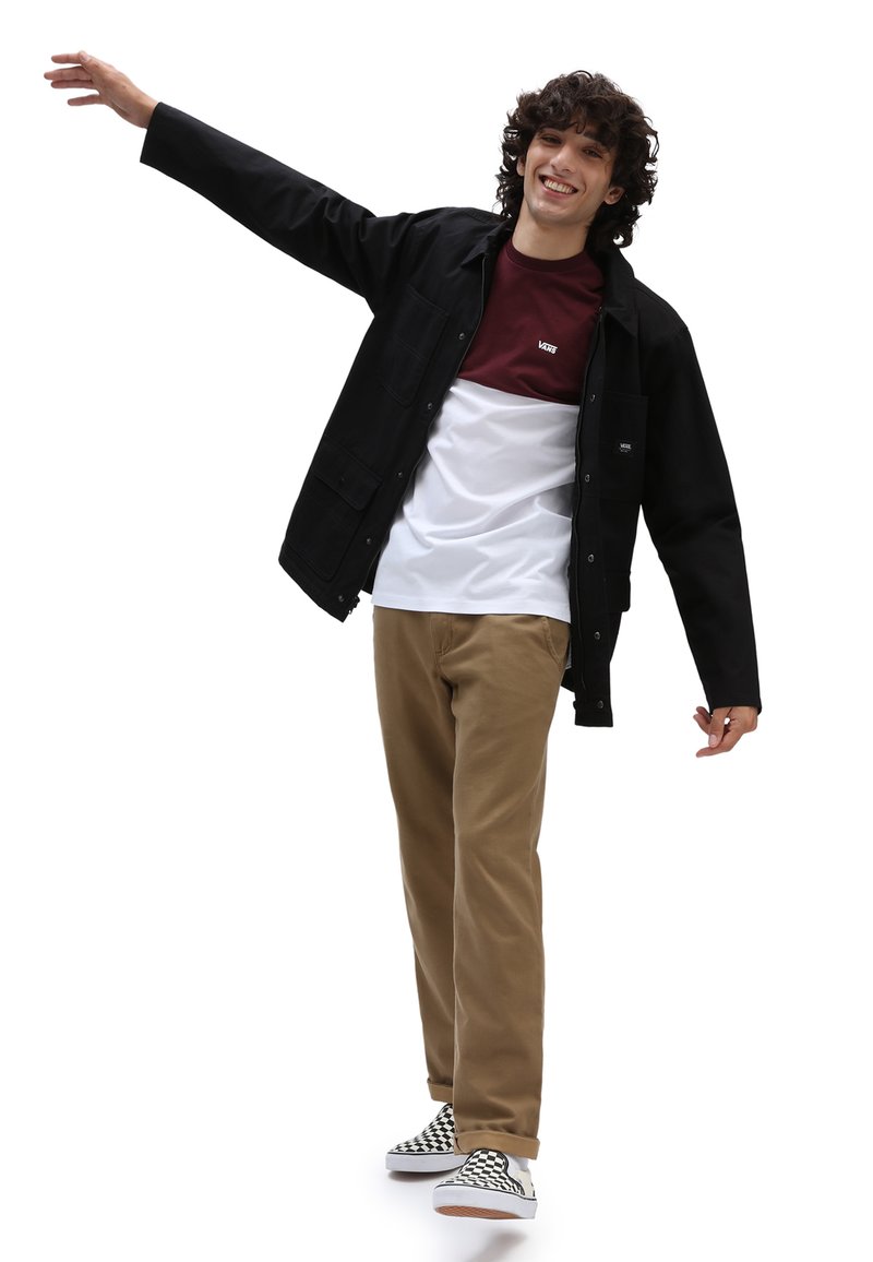 Black jacket over a maroon and white T-shirt, worn with khaki pants and checkered slip-on shoes; model posing with one arm raised.