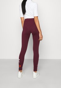 Maroon leggings with a smooth texture, featuring floral embroidery along the sides and an elastic waistband. Paired with white sneakers.