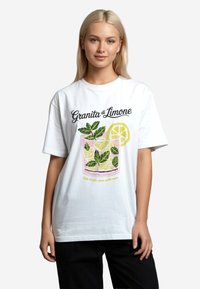 Bílý tričko s barevným grafickým motivem nápoje s plátky citronu a mátovými listy, s textem "Granita di Limone" nad tím.