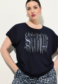 Námořnické tričko s krátkým rukávem, na kterém je velký kovový potisk "STYLE". Měkká tkanina s volným střihem, v kombinaci s vzorovanými kalhotami.