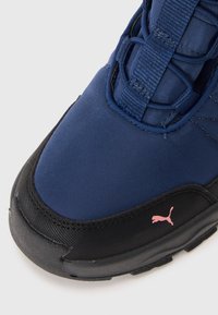 Blauwe sneakerneus met zwarte rubberen zool en roze Puma-logo aan de buitenrand, voorzien van vetersluitingen en een bovenwerk van textuurstof.