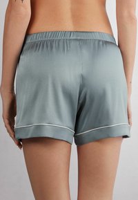 Světlé šedé saténové kraťasy s elastickým pasem, s přehnutým lemem a bílým lemem podél spodního okraje. Hladká textura.