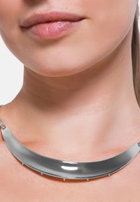 Collier ras du cou en métal au design courbé et brillant. Il présente une finition argentée lisse et contient plusieurs petits accessoires.