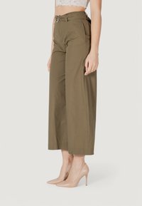 Pantaloni a gamba larga color khaki con vita cintura, tasche laterali e una texture di tessuto liscia, abbinati a scarpe con tacchi alti color nude.