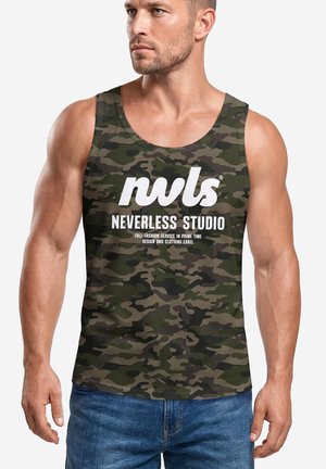 Muskelbepackter Mann trägt grünes und braunes Camouflage-Trägershirt mit weißem "nvls NEVERLESS STUDIO" Text, kombiniert mit blauen Jeans.