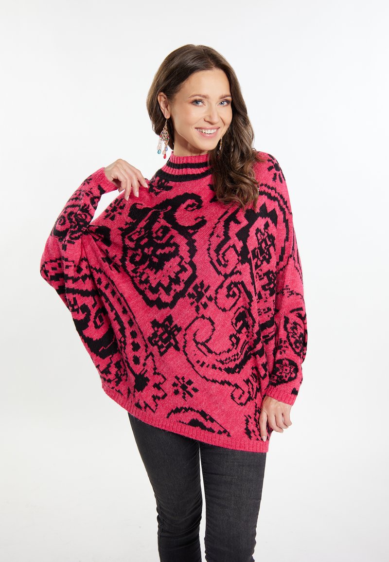 Rosa übergroßer Pullover mit schwarzen, filigranen Blumenmustern, Rundhalsausschnitt, gerippten Bündchen und einem strukturierten Strickdesign. Kombiniert mit dunklen Jeans.
