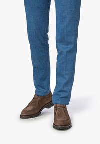 Scarpe stringate in suede marrone con suola in gomma, abbinate a pantaloni blu testurizzati. Le scarpe hanno una punta arrotondata e dettagli di cucitura discreti.