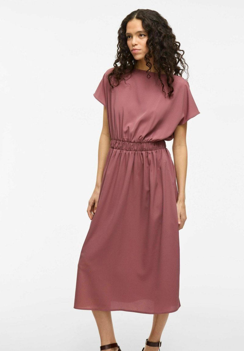 Mavčno obleko s kratkimi rokavi in elastičnim pasom, ki ima valovito, krilo do kolen in mehko, gladko teksturo tkanine.