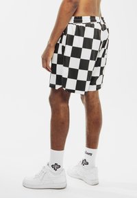 Shorts a scacchi bianco e nero, realizzati in tessuto elegante, con vita elastica e tasche laterali, indossati con sneaker e calze bianche.