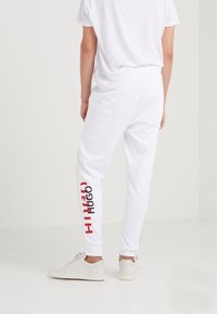 Witte joggers van zacht materiaal, met een aansluitend ontwerp en het rode "HUGO" logo verticaal afgebeeld op het linkerbeen.