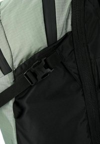 Primer plano de un cierre de plástico negro que sujeta una correa ajustable en una bolsa de tela gris y negra con un cierre visible.