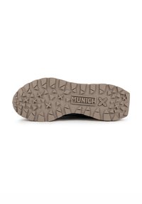 Semelle de chaussure de sport noire avec un motif texturé et robuste et des crampons de traction bien marqués. Présente le nom de la marque « MUNICH » embossé sur le côté.