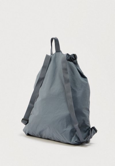 Γκρι σακίδιο πλάτης με κορδόνι, κατασκευασμένο από ελαφρύ ύφασμα, με ρυθμιζόμενους ιμάντες και σφιχτό πάνω μέρος, με λεία υφή και μίνιμαλ σχεδιασμό.