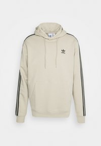 Beige hoodie i bomullsblandning med känguruficka, svarta tre ränder på ärmarna och en liten svart logotyp på bröstet.