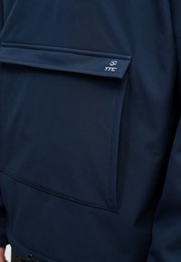 Tengerészkék dzseki cipzáras zsebbel, sima textil felülettel és minimális arculati elemekkel az elülső részen, a letisztult megjelenés érdekében.