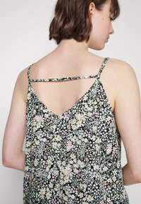 Top sem mangas com padrão floral, apresentando um fundo preto com flores em tons pastéis, costas em forma de V e alças finas com um detalhe decorativo em entrelaçado.