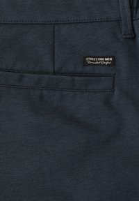 Pantalon homme bleu foncé avec une poche arrière portant une petite étiquette noire cousue dessus indiquant « Street One Men Unmatched Comfort ».