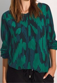 Zielona i ciemno-skalna bluzka w wzory o luźnym kroju, z długimi rękawami i mankietami, charakteryzująca się miękką teksturą i subtelnym połyskiem.
