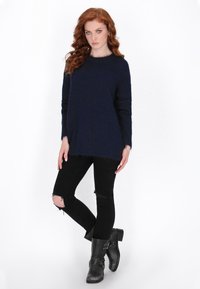 Marineblauer Strickpullover mit Rundhalsausschnitt, kombiniert mit schwarzen, verwaschenen Jeans und schwarzen Stiefeletten mit doppelten Schnallen.